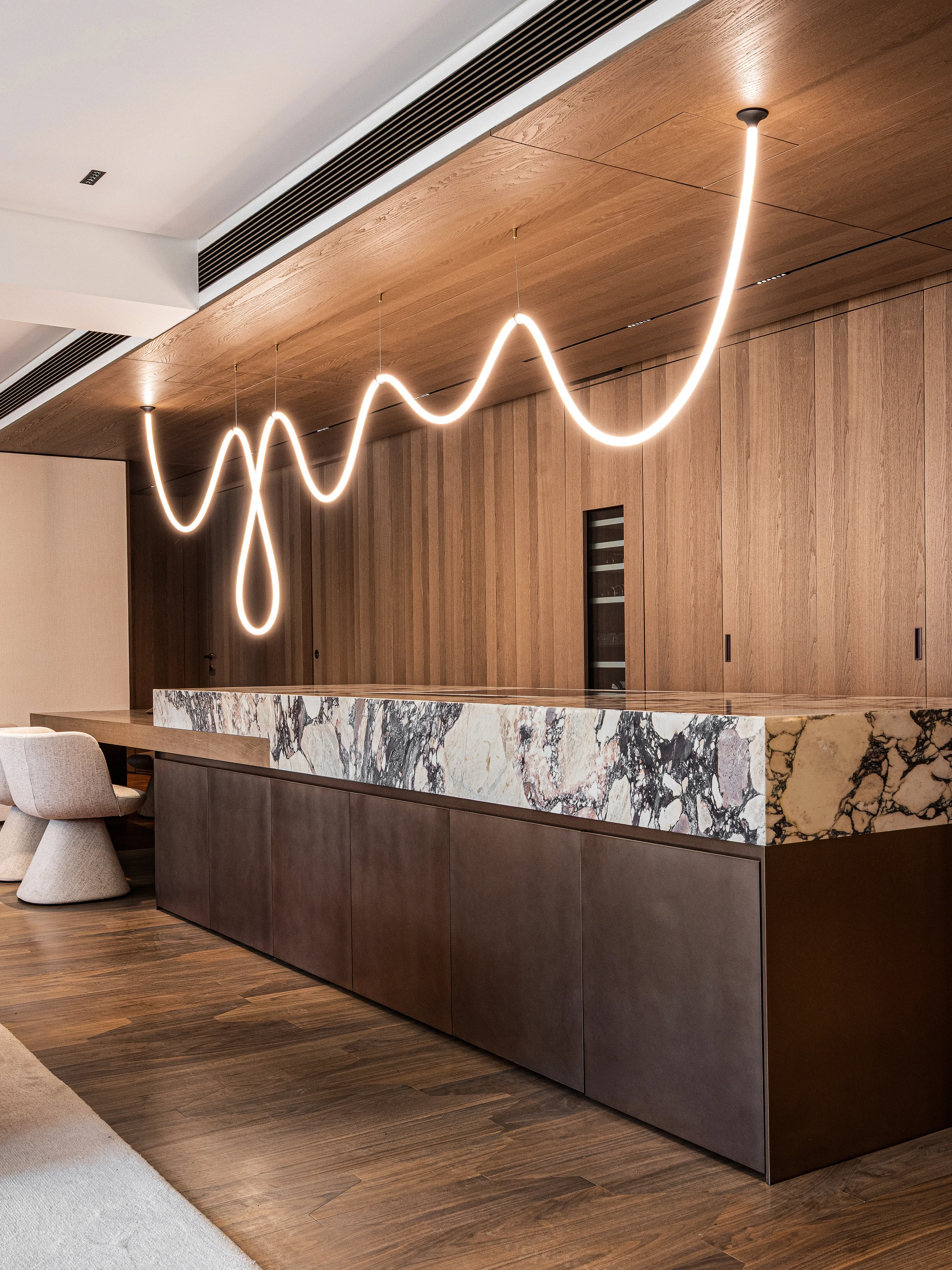 Marble-topped kitchen island with bronze cabinetry and wavy pendant light, The Amber Residence, Beijing