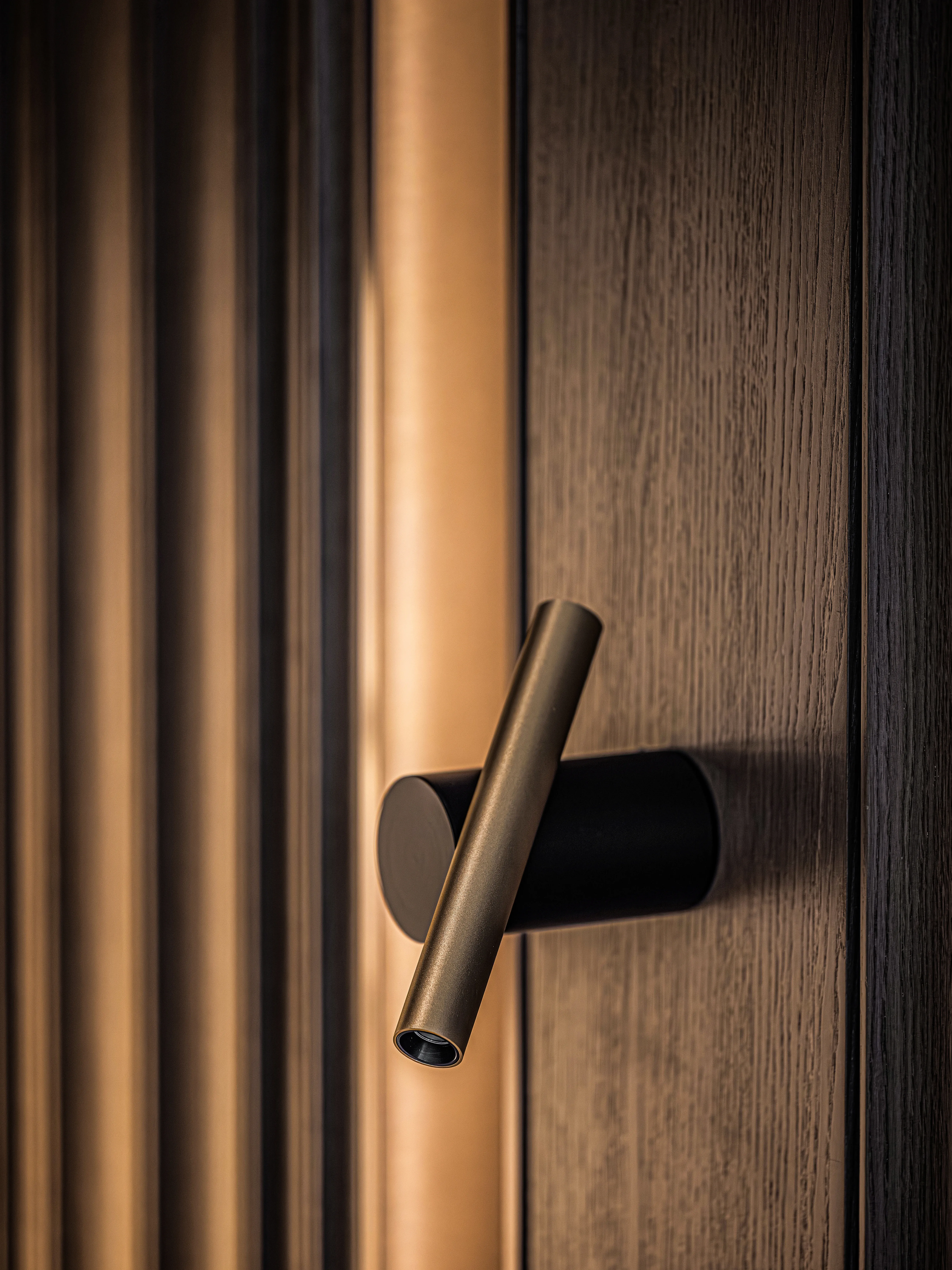 Close-up of bronze cylindrical handle on fluted wood door panel, The Amber Residence, Beijing